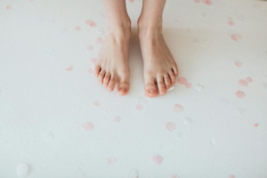 Bare feet with visible toenails against a white background with scattered pink confetti.