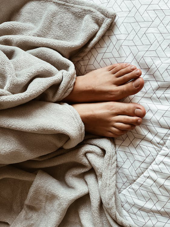 Addressing FAQs About Toenail Fungus Laser Therapy Feet peeking out from a cozy blanket.