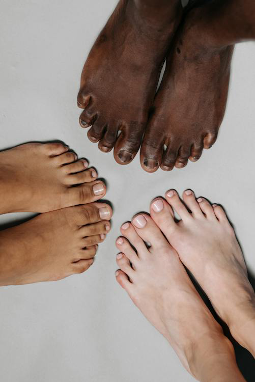 Several pairs of feet closely together, varying in skin tone and nail condition.