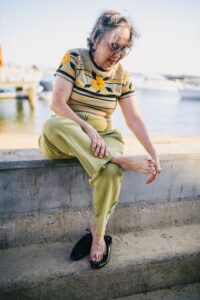 Can Sweaty Feet Cause Toenail Fungus? Here’s What You Need to Know An individual sitting by the waterfront, inspecting their foot.