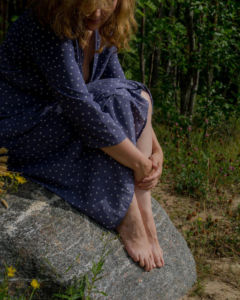 A person sitting on a rock in a natural outdoor setting, holding their bare feet.